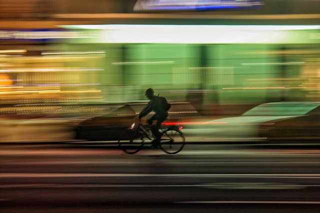 A heavily motion-blurred image of a biciclyst on a city street at night